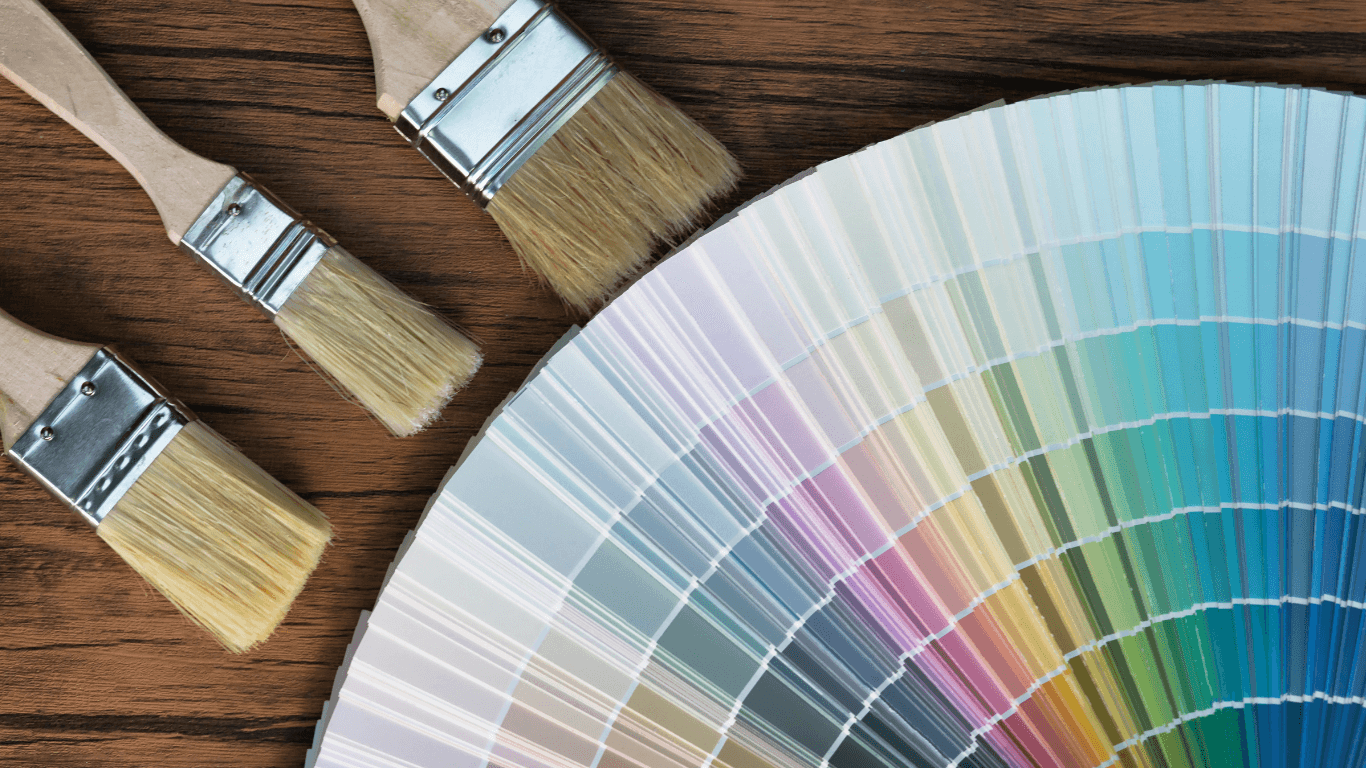 Paintbrushes and a color fan deck arranged on a wood table