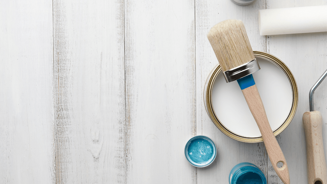 Open paint can, brush, and roller on a light wood surface